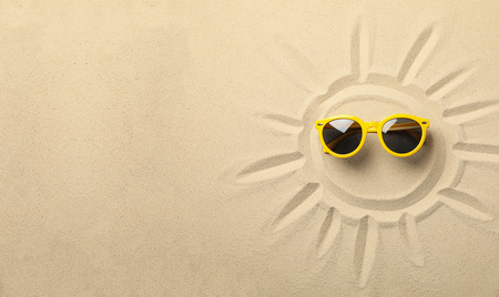 In Sand gezeichnete Sonne, darin eine gelbe Sonnenbrille