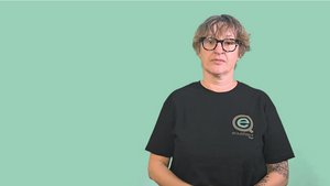 Screenshot aus einem der ÖGS-Videos dieses Newsbeitrages: Frau mit kurzen dunkelblonden Haaren, in schwarzem T-Shirt mit equalizent-Logo steht vor einem helltürkisen Hintergrund.