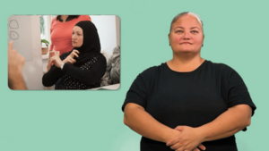 Frau mit schwarzem Shirt steht mit verschränkten Händen vor einem türkisen Hintergrund. Neben ihr ist ein Foto eingeblendet, das eine Frau mit Kopftuch zeigt, die "Österreich" gebärdet.
