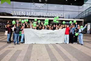 equalizent Kursteilnehmer*innen und -Mitarbeitende stehen hinter einem großen Transparent auf dem "I steh auf Gebärdensprache" steht. Im Hintergrund ist der Schriftzug "Hauptbahnhof" zu sehen.