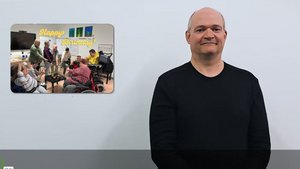 Screenshot des ÖGS-Videos. Rechts steht ein Mann mit schwarzem Shirt und gebärdet etwas. Links von ihm ist ein Foto mit 2 meditierenden Frauen zu sehen. Darunter steht: 23.10.2025, 17:00 bis 19:00 Uhr"