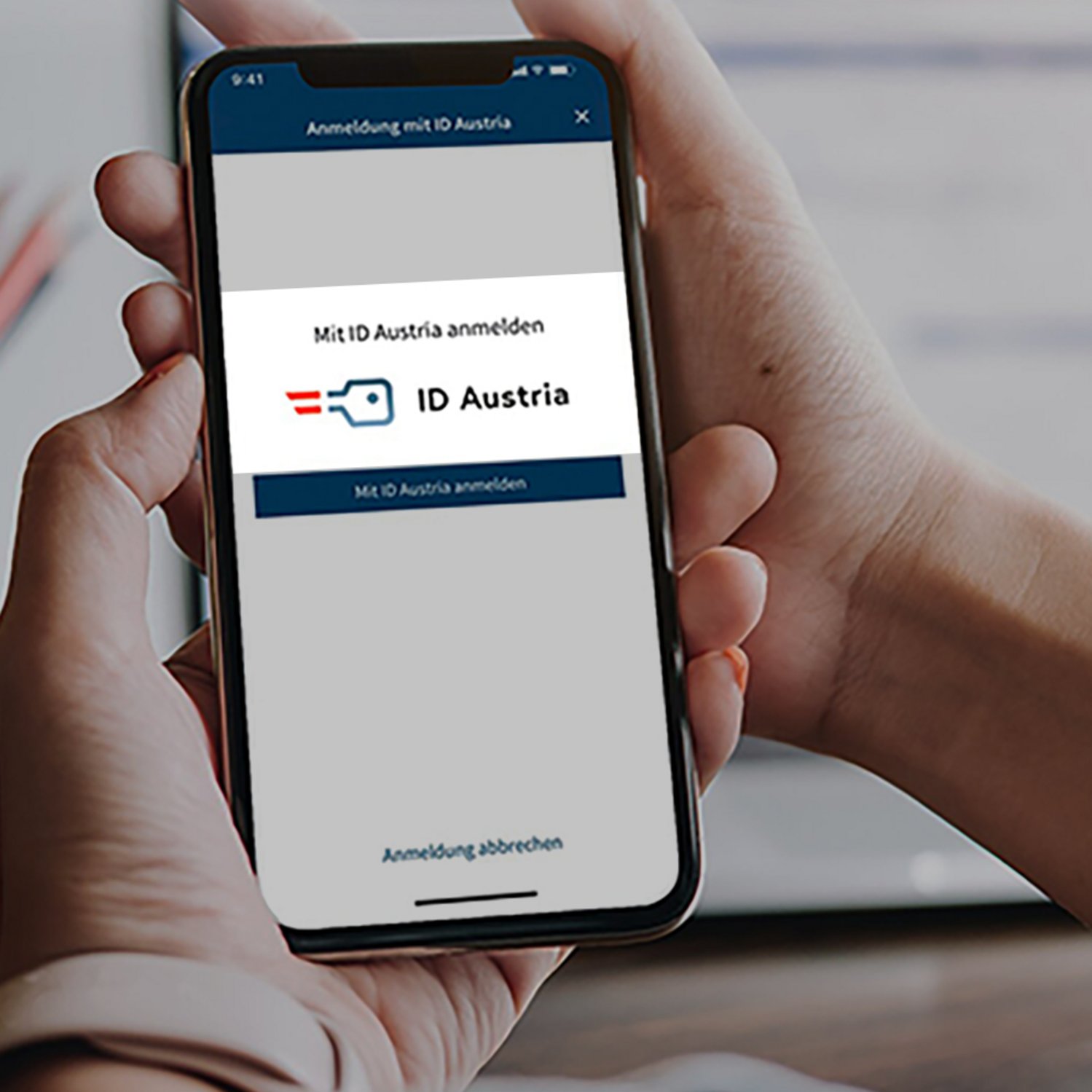 Smartphone, das von 2 Händen gehalten wird. Auf dem Bildschirm ist das Logo von ID Austria zu sehen.