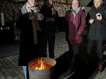 Vier Kursteilnehmende stehen im Garten des equalizent mit Punschtassen in der Hand und wärmen sich an einem kleinen Feuer