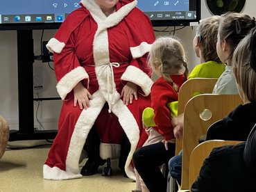 Eine als weihnachtsfau verkleidete Mitarbeiterin des equalizent sitzt vor Sesselreihen mit Kindern.