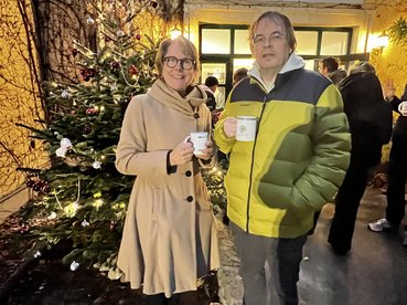 Marietta Adlbrecht steht mit Dieter Chmiel vom Sozialministeriumservice mit Punschtassen vor dem Eingang des equalizent.