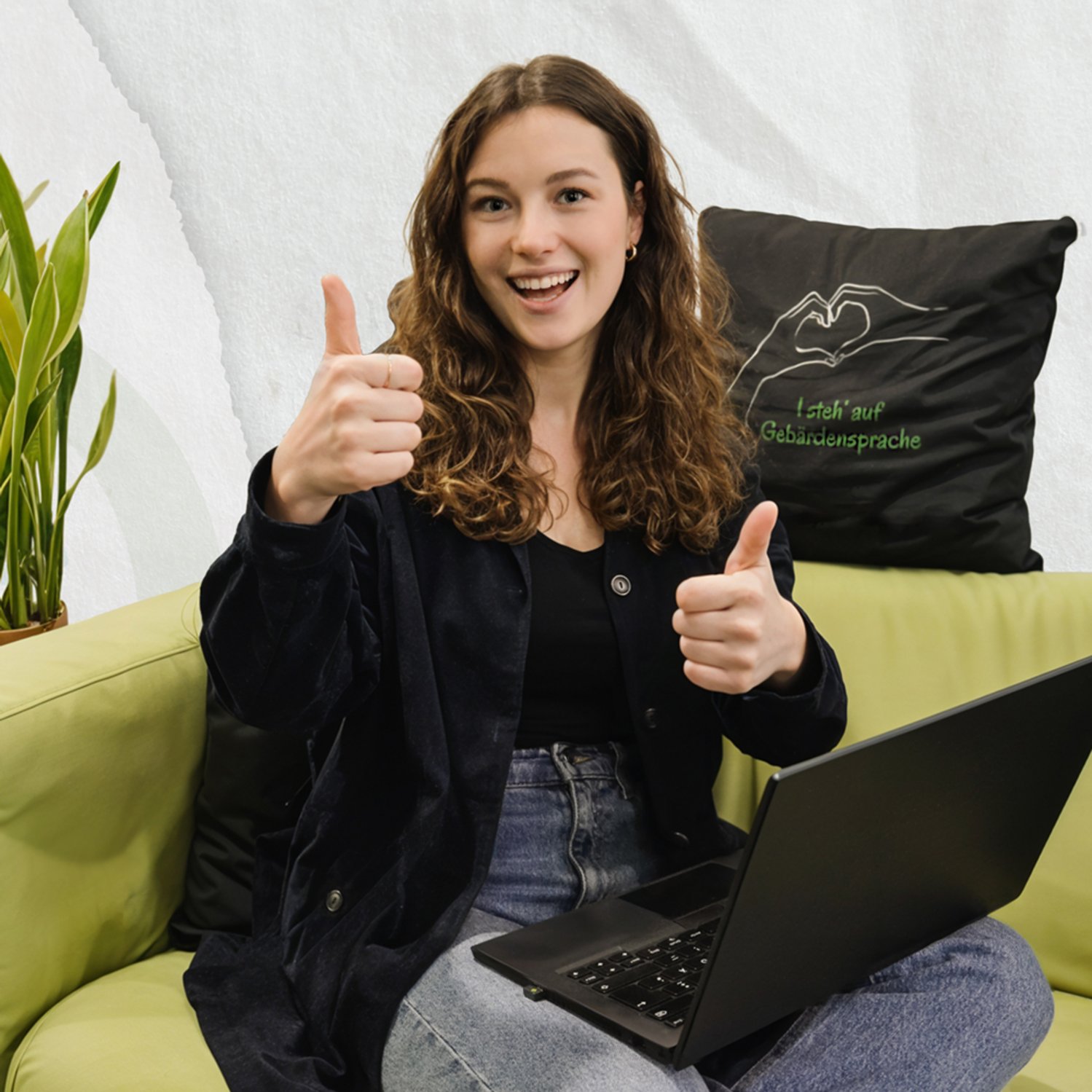 Frau sitzt am Sofa mit einem Laptop am Schoß und zeigt "Daumen hoch"