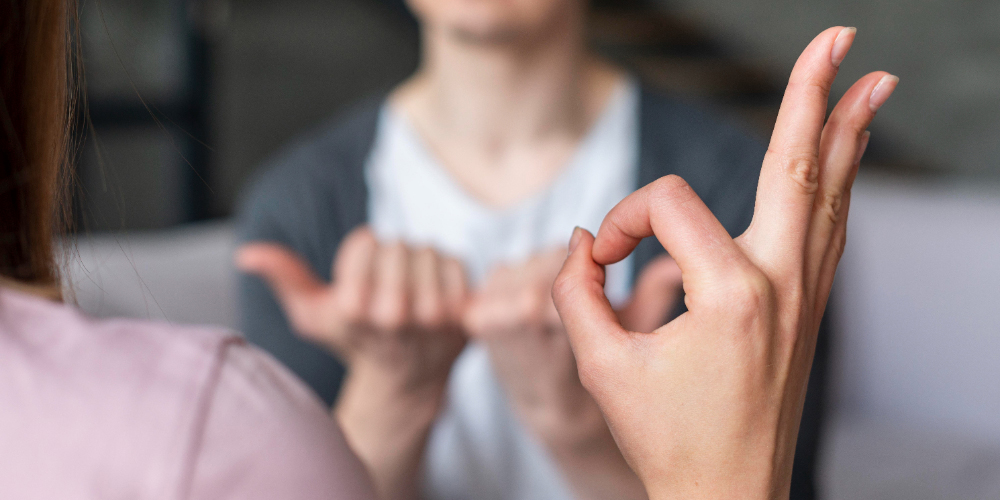 Hand gebärdet "gut", im Hintergrund sieht man eine weitere Person, die ebenfalls etwas gebärdet