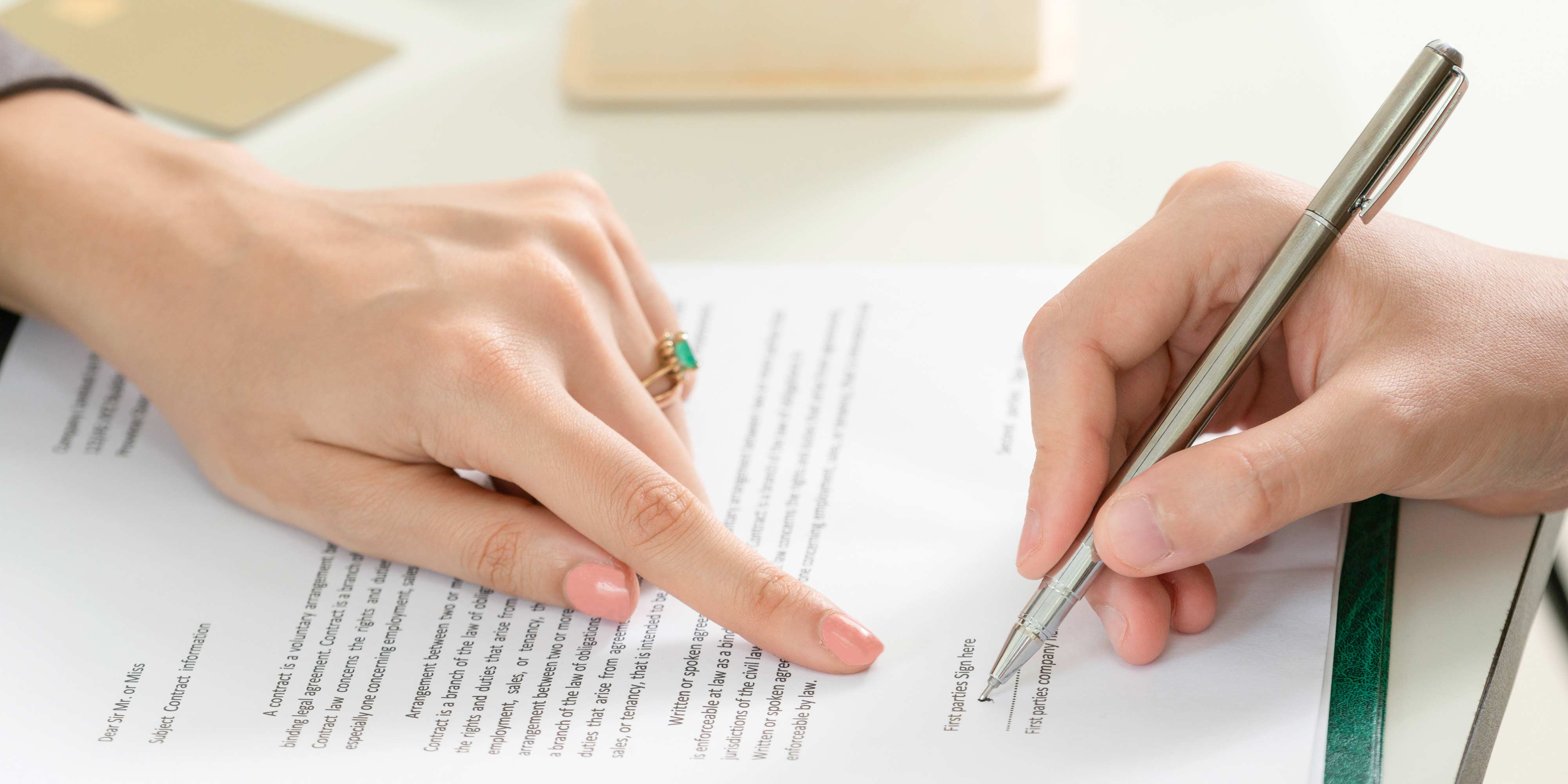 Eine Hand unterschreibt einen Vertrag, die andere zeigt mit dem Finger, wo genau zu unterschreiben ist.