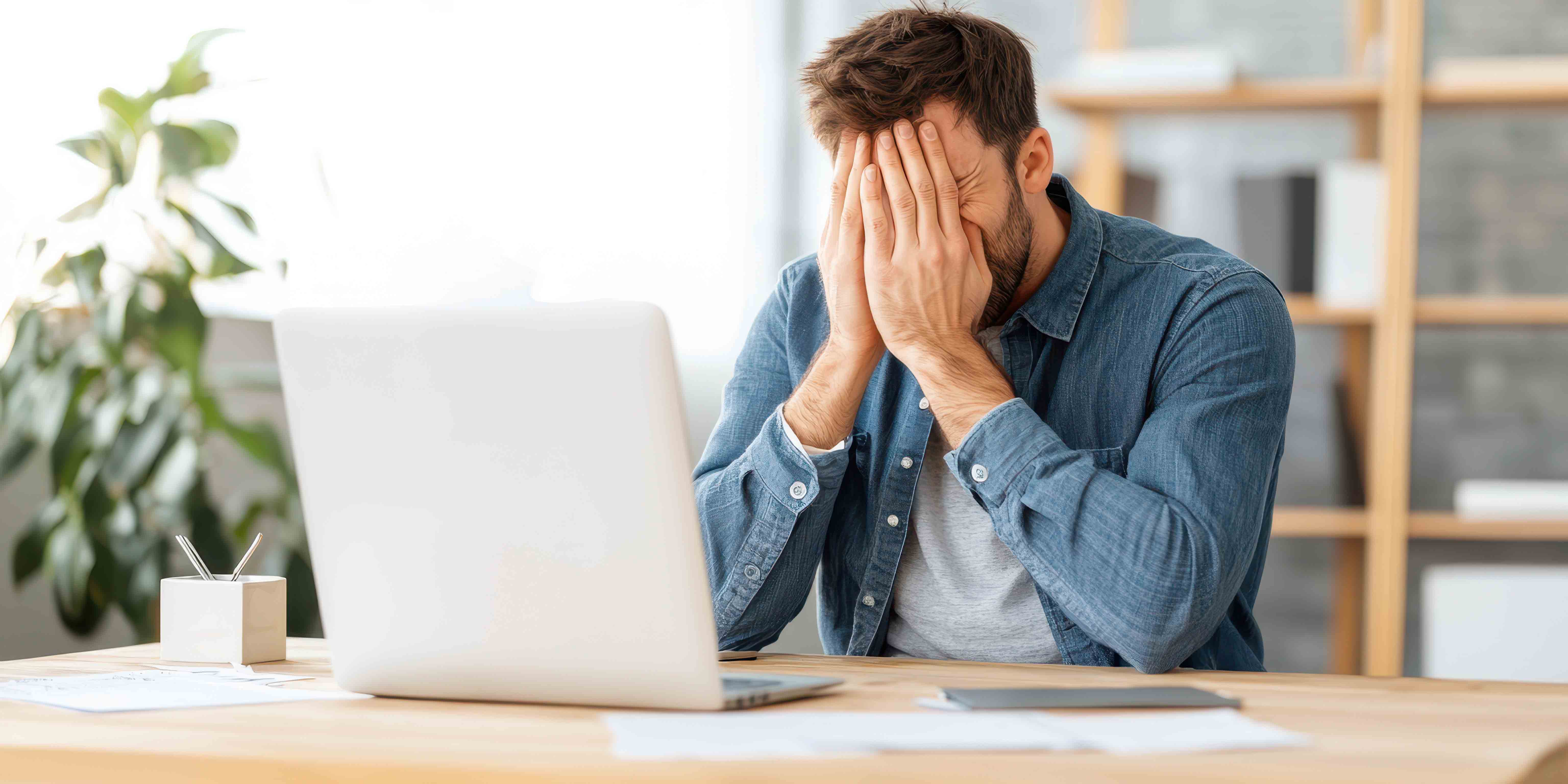 Mann sitzt gestresst vor einem Laptop mit den Händen vor dem Gesicht