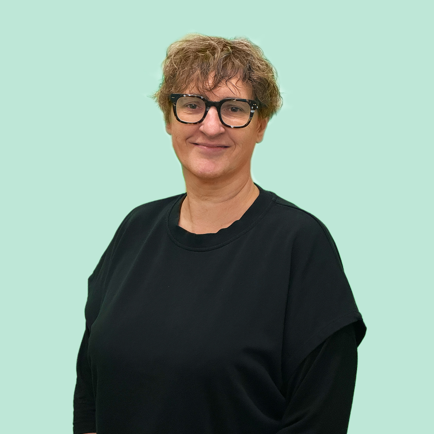 Frau mit kurzen blonden Haaren und Brille mit schwarzem Shirt bekleidet